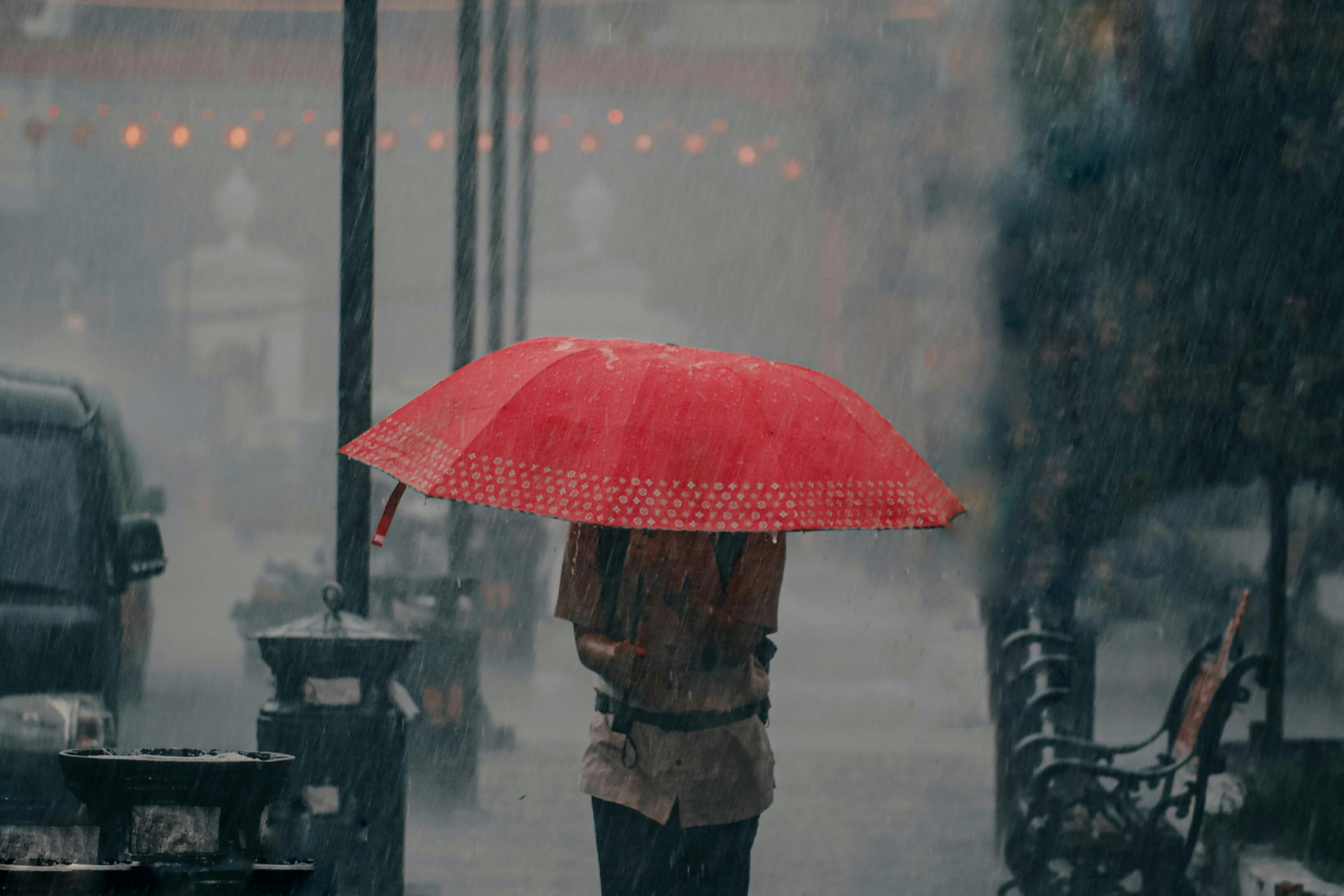 man running in rain storm with red umbrella