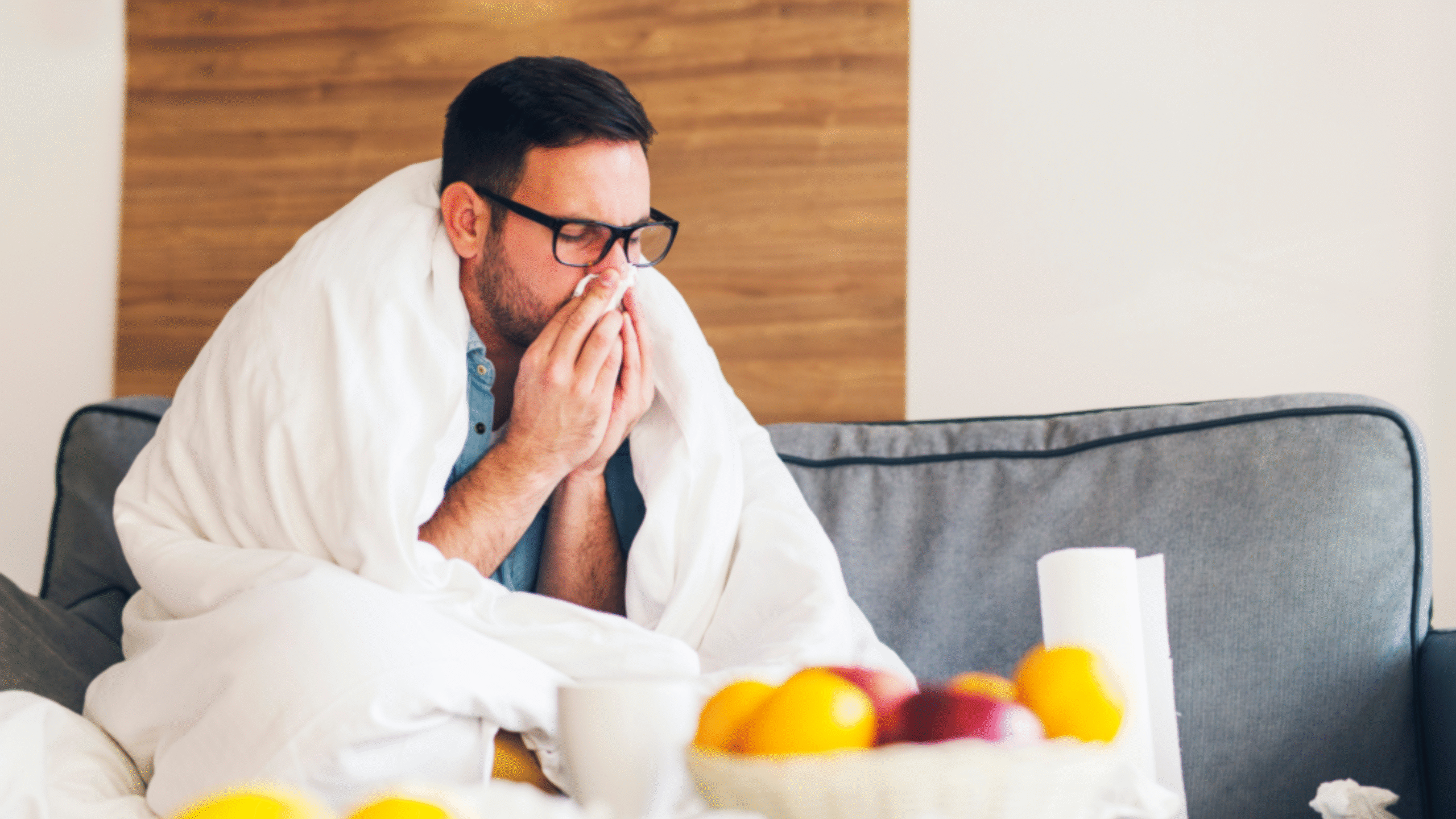 Man sick on the couch blowing his nose and bundled up on the couch